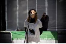 Esther Mischke trägt eine schwarze Kappe und ein bedrucktes T-Shirt. Sie spricht in ein Mikrophon. Hinter ihr sind Teile der iranischen Flagge zu sehen.