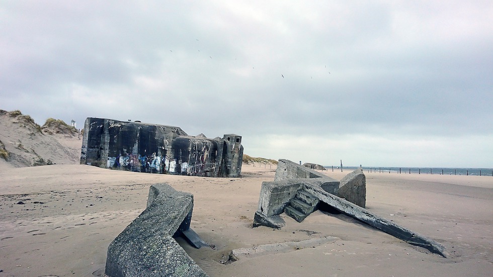 Betonbunker an der Westküste An einem Strand liegen zum Teil im Sand vergrabende Überreste eines Betonbunkers.