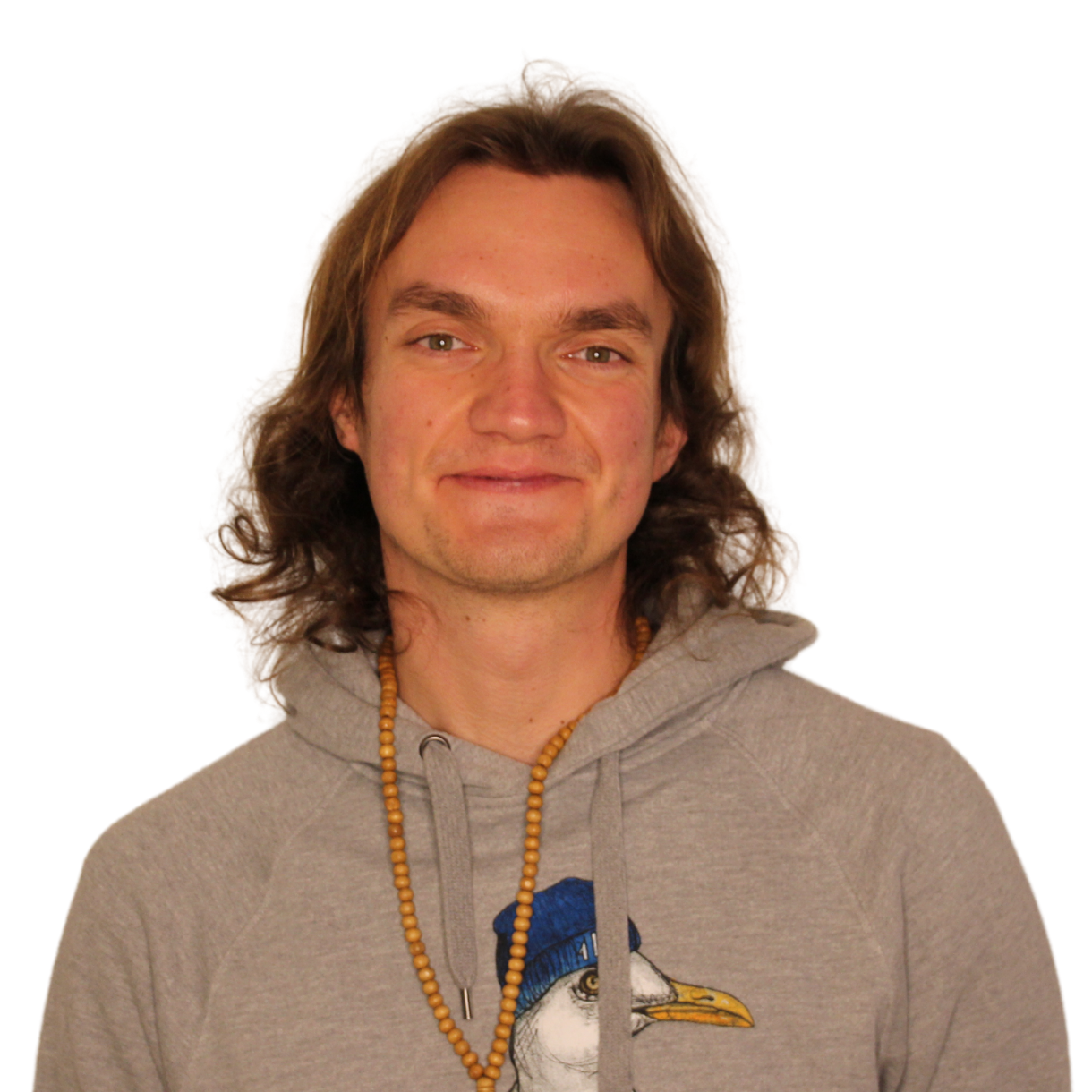 David_Schenk Porträt von David Schenk. Ein junger Mann mit schulterlangen braunen Haaren lächelt in die Kamera. Er trägt einen grauen Hoodie und eine Holzperlenkette um den Hals.