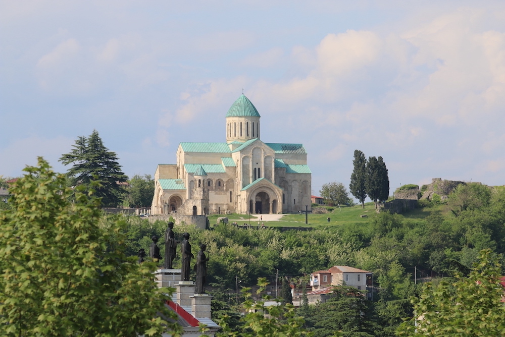 Eine weiße russisch-orthodoxe Kirche mit grünem Kupferdach steht auf einem Berg in Georgien.