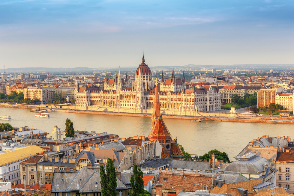 Das Parlament in Budapest von der gegenüberliegenden Wasserseite aus. Zu sehen sind viele historische Gebäude drum herum.