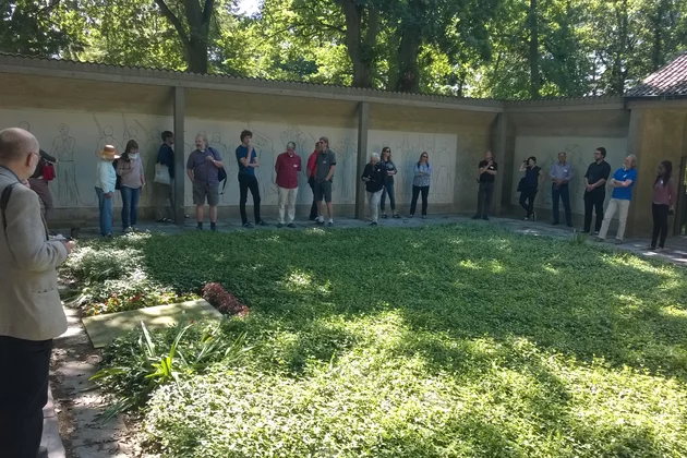 Teilnehmende der Landesgedenkstättentagung 2016 in Lübeck stehen um einen bewachsenen Platz herum.