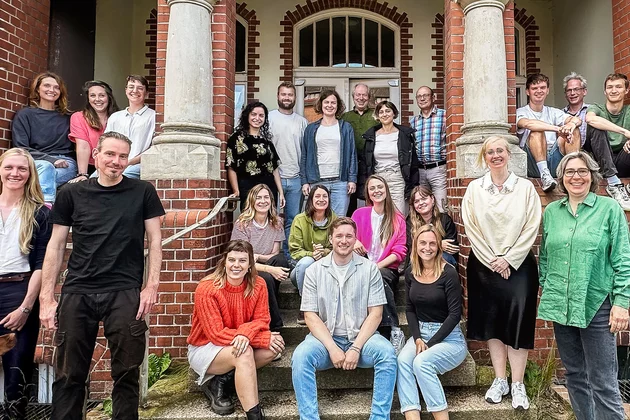 Teamfoto der Böll-SH. Etwa 20 Personen sitzen und stehen vor dem Eingang ihres historischen Bürogebäudes im Anschaspark Kiel.