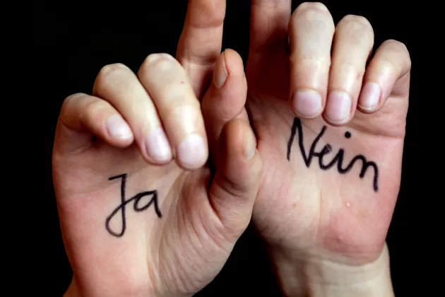 Zwei Hände vor einem schwarzen Hintergrund. Auf den Innenflächen der Hand steht jeweils ja und nein geschrieben.