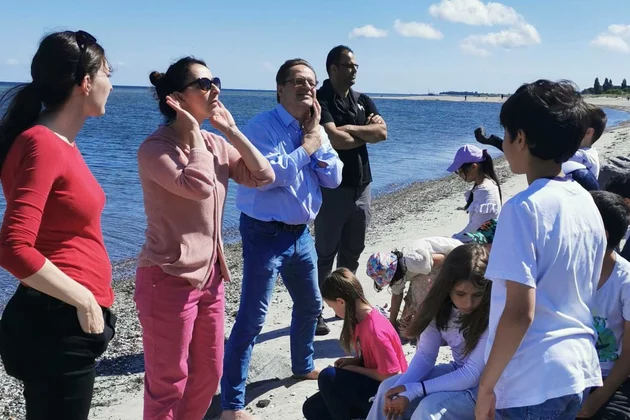 Am Strand in Kiel machen die Teamleiter der Kinderoper den teilnehmenden Kindern etwas vor.