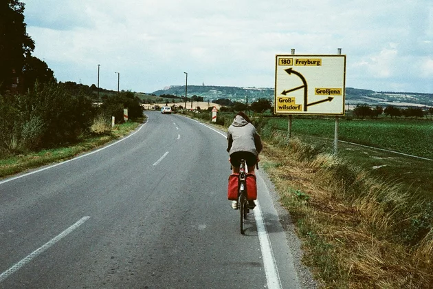 Auf einer Straße in der ehemaligen DDR fährt ein Radfahrer. Vor ihm ist ein Straßenschild, das den Weg angibt.