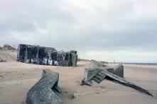 An einem Strand liegen zum Teil im Sand vergrabende Überreste eines Betonbunkers.