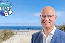 Porträt von Schleswig-Holsteins Umweltminister Tobias Goldschmidt. Im Hintergrund ist ein Strand und Meer. Links oben ist das Logo vom Ocean Five Podcast.