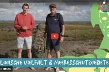 Elias (frutti di mare) und Claus von Hoerschelmann (Multimar Wattforum) stehen gemeinsam im Watt der Nordsee. Rechts ist eine grüne Landkarte vom Gebiet des Nationalparks Wattenmeer.