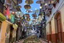 Eine Straße in La Paz, Bolivien ist mit vielen Regenschirmen und Lichterketten überhangen. Auf dem Boden ist aufgeschlagener Steinboden.