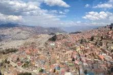 La Paz, Bolivien, von oben. Unzählige Häuser liegen an einem Hang. Am Horizont sind Berge und blauer, mit weißen Wolken durchzogener Himmel.