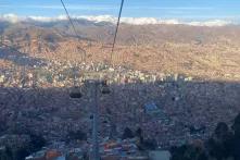 La Paz, Bolivien, aus der Seilbahn von oben. Unten sind unzählige Häuser, am Horizont sind Berge, an denen weiße Wolken hängen.