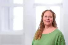 Potrait von Stefanie Sudhaus. Sie trägt ein hellgrünes Oberteil. Sie hat lange lockige rotblonde Haare und lächelt in die Kamera.