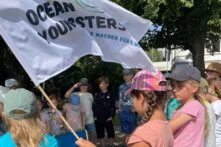 Meermacher Woche. Eine Gruppe von Kindern zwischen 8 und 12 Jahren steht in einem Kreis. Ein Kind hält eine große Fahne mit der Aufschrift "Ocean Youngsters".