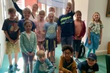 Eine Gruppe an Kindern steht nebeneinander in die Kamera blickend. Sie lächeln. Vor den stehenden Kindern sitzen drei Kinder in der vorderen Reihe. Eines der Kinder in der hinteren Reihe hält eine Fahne mit der Aufschrift "Ocean Youngsters". Es handelt sich hierbei um die Teilnehmenden der Meermacher Woche.