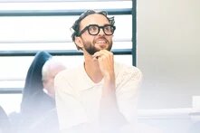 Eine Person schaut lächelnd in die Höhe. Sie sitzt auf einem Stuhl.