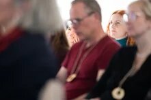 Einige Menschen sitzen konzentriert auf Stühlen und hören bei einem Vortrag zu.