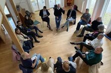 Eine Gruppe an Menschen sitzt in einem Kreis zusammen auf Stühlen.
