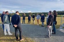 Eine Gruppe an Menschen steht auf einem Kiesweg in einem Kreis zusammen und hört einer sprechenden Person zu.