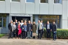Eine Gruppe an Menschen steht vor einem Gebäude. Auf dem Gebäude steht "Mercatorstr. 3".