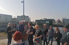 MehrereLeute machen eine Tour durch die Stadt. Im Hintergrund ist die Stadt zu sehen. Im Vordergrund eine Gruppe von Menschen und eine vortragende Person.