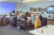 Eine Gruppe an Personen sitzt an einem großen Tisch zusammen. Sie scheinen sich zu unterhalten.