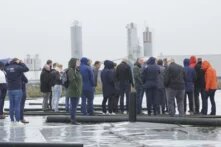 Eine Gruppe an Menschen steht im Regen in der Stadt auf einem Erdbeckenspeicher.