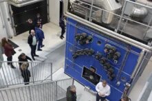 Eine Personen stehen vor einer riesigen Maschine. Es handelt sich hierbei um einen Biomassekessel.