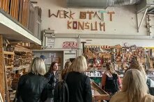 Personen stehen in einer Holzwerkstatt, die Werkstattkonsum heißt.