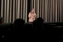 Maria Birger, Mitarbeiterin des Böll-Archivs, steht in einem Kinosaal, in dem Die verlorene Ehre der Katharina Blum gezeigt wird, und trägt vor dem Vorhang etwas vor.