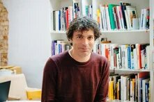 Davide Brocchi sitzt vor einem Bücherregal.