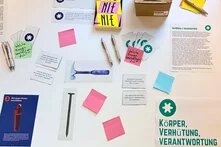 Feministische Werkstatt in Kiel: Ein Tisch voller Schreibmaterialien. Ein Zettel mit der Aufschrift "Körper, Verhütung, Verantwortung"