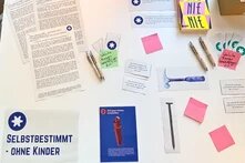 Feministische Werkstatt in Kiel: Viele Zettel und Stifte liegen auf einem Tisch, um damit zu arbeiten. Es liegen Texte daneben und ein Zettel mit der Aufschrift "Selbstbestimmt – ohne Kinder"