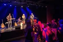 Feministische Werkstatt in Kiel: Tanzende Menschen vor einer Bühne, auf der eine Band Musik macht.