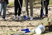 Vier Jugendliche sammeln Müll am Strand mit Müllzangen.
