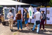 Personen stehen vor hängenden Bannern und stehen vor einer Karte an einer Pinnwand. Sie unterhalten sich.