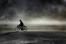 Ein Mann mit einem Fahrrad fährt vor einer in Nebel oder Gas verhangenen Stadt