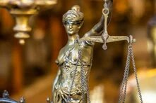Es wird eine Justicia-Figur in goldener Farbe im Anschnitt dargstellt. Der Hintergrund ist verschwommen.