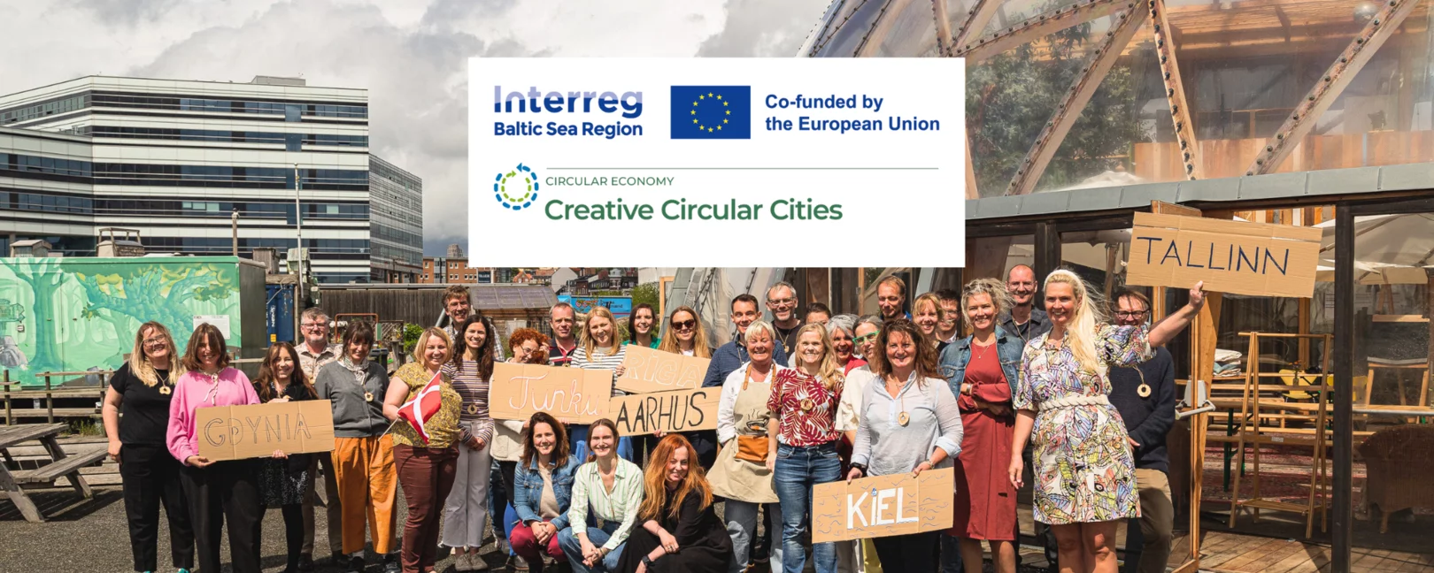 Logo von Creative Circular Cities. Im Hintergrund stehen zahlreiche Projektpartner*innen vor einer Kuppel in Aarhus.