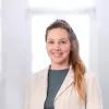 Janina Löwe Portrait von Janina Löwe. Eine junge Frau mit langen blonden Haaren lächelt in die Kamera. Sie trägt ein graues Shirt unter einem cremefarbenen Blazer.