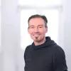 Portrait von Peter Wiebe. Ein mittelalter Mann mit kurzen grau-braunen Haaren. Er hat einen Dreitagebart und trägt einen schwarzen Hoodie.