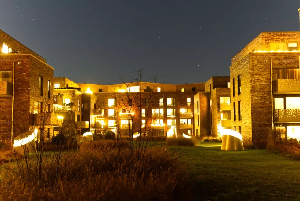Ein Wohnblock in der Dunkelheit. Alle Fenster sind hell erleuchtet und verbreiten gelbes Licht.