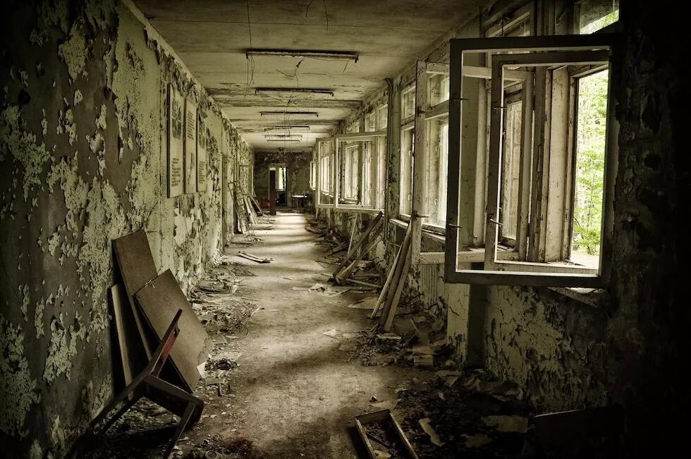 Zerstörter Flur in Tschernobyl Zu sehen ist ein zerstörter Flur. Von den Wänden blättert Farbe ab, auf dem Boden liegt Abfall. Auf der rechten Seite ist eine Fensterfront. Die Fenster stehen offen und haben kein Glas mehr. Der Flur ist Teil eines Gebäudes in Tschernobyl.