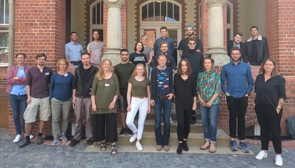 Ocean Summit Hackathon Eine Gruppe vieler Menschen steht vor einem historischen Backsteingebäude. Alle schauen in die Kamera.