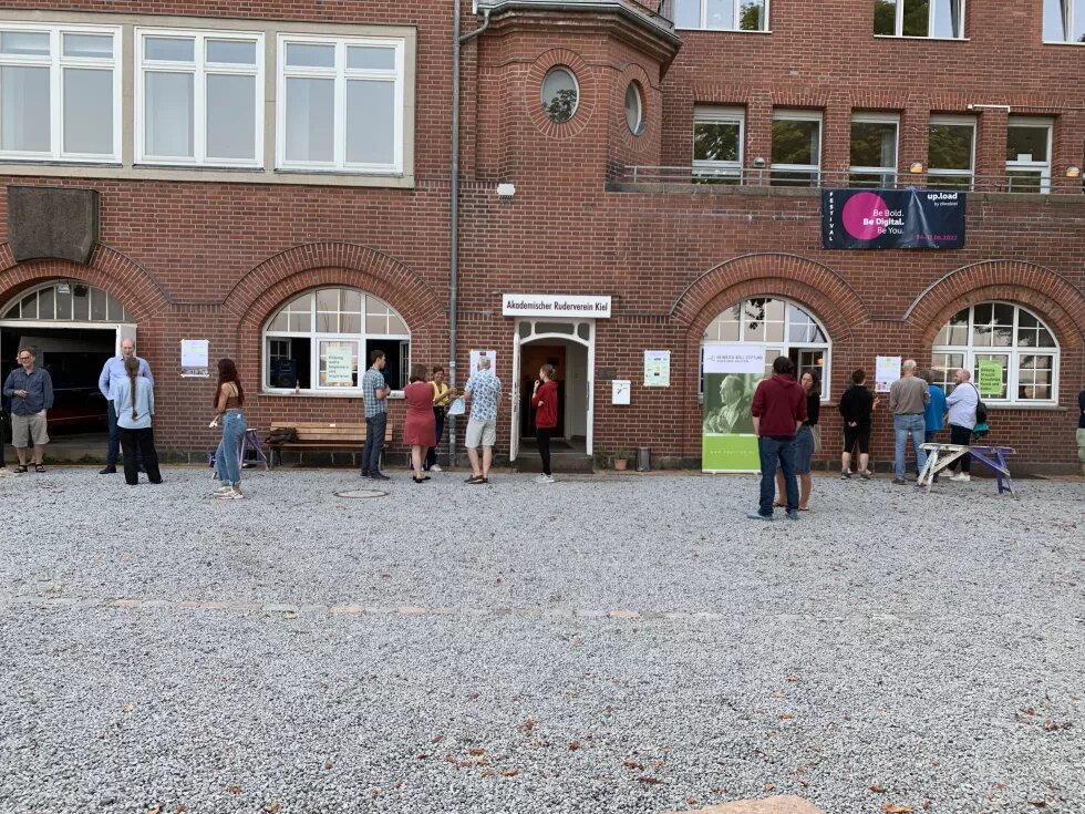 Sommerfest Mehrere Leute stehen vor einem Backsteingebäude. Neben dem Eingang steht ein Plakat der Heinrich-Böll-Stiftung Schleswig-Holstein.
