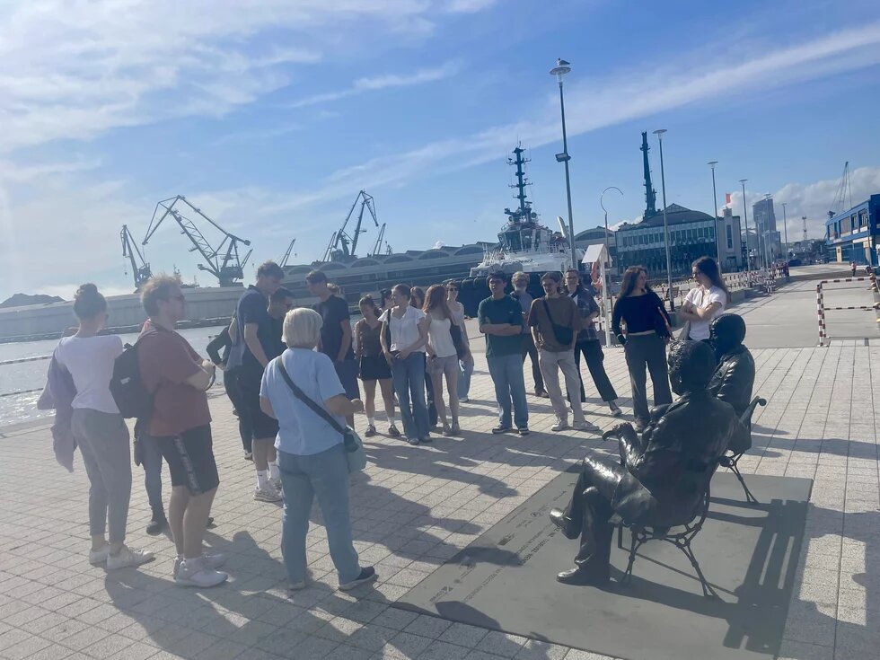 Die Reisegruppe Gedenkstättenfahrt 2025 steht an einem Kai in Gdynia. Eine Stadtführerin erklärt etwas.