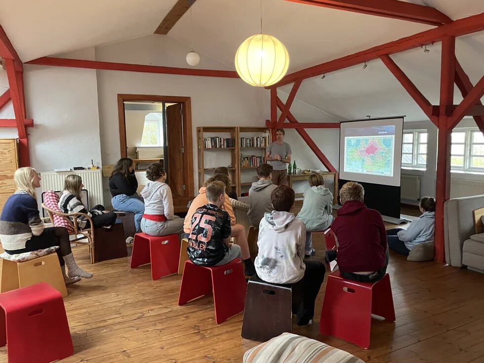Beim MeerMach-Camp sietzen Schüler*innen auf Hockern und hören einem Vortrag zu.
