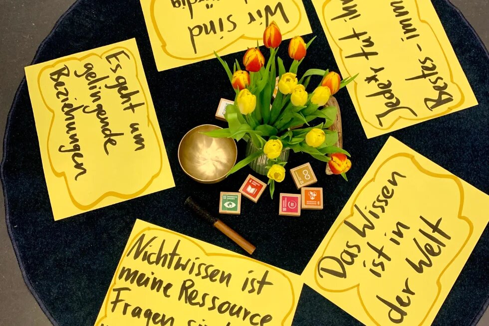 Auf gelben Zetteln stehen Leitsätze des Changemaker-Ansatzes. In der Mitte steht eine Vase mit Tulpen.