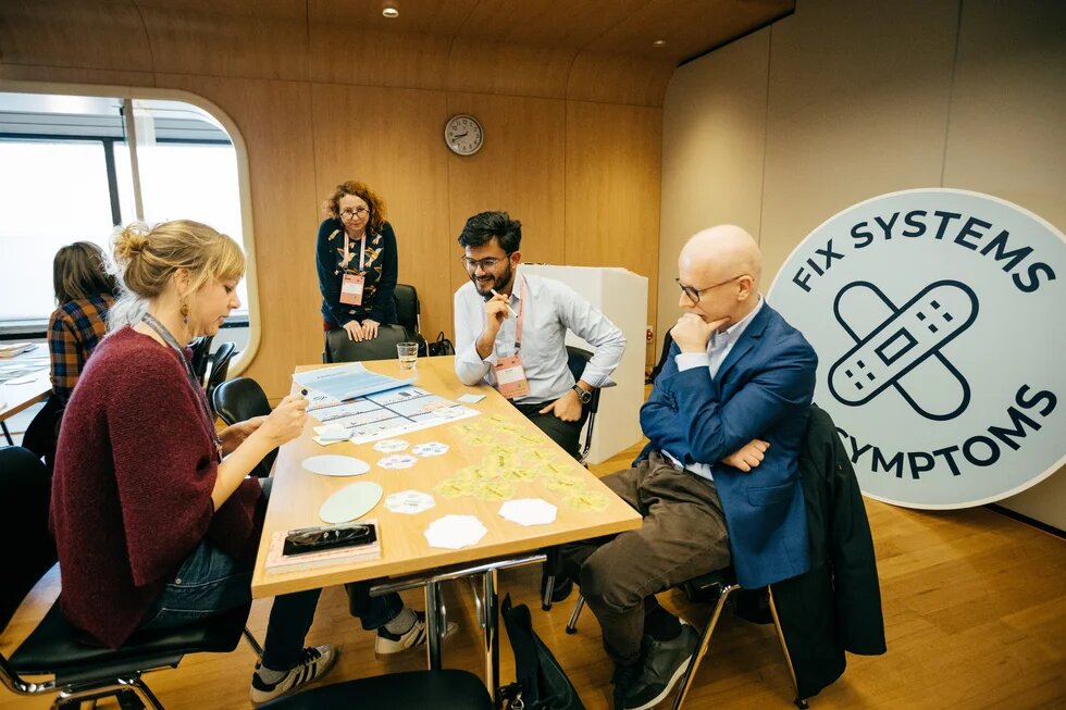 Vier Personen sitzen beim Workshop um einen Tisch herum. Auf dem Tisch liegen Karten, die sie sich anschauen.