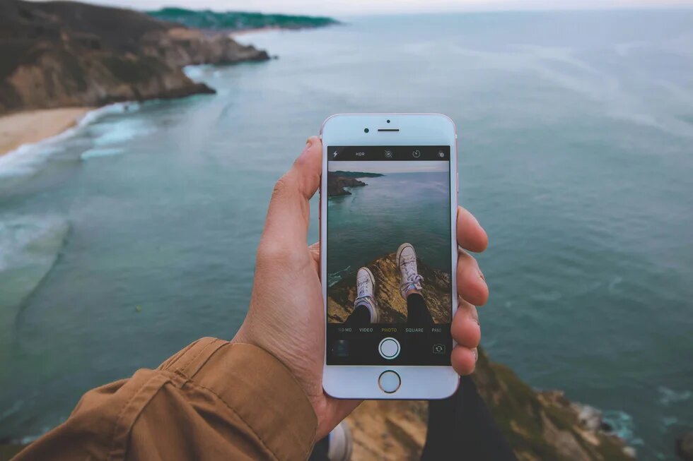 Smartphone in der Hand filmt Füße und das Meer.